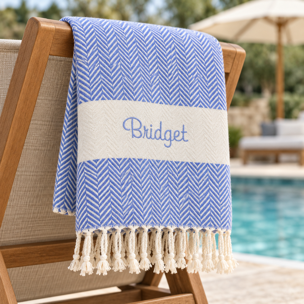 Blue herringbone Turkish towel embroidered with Bridget beside a pool