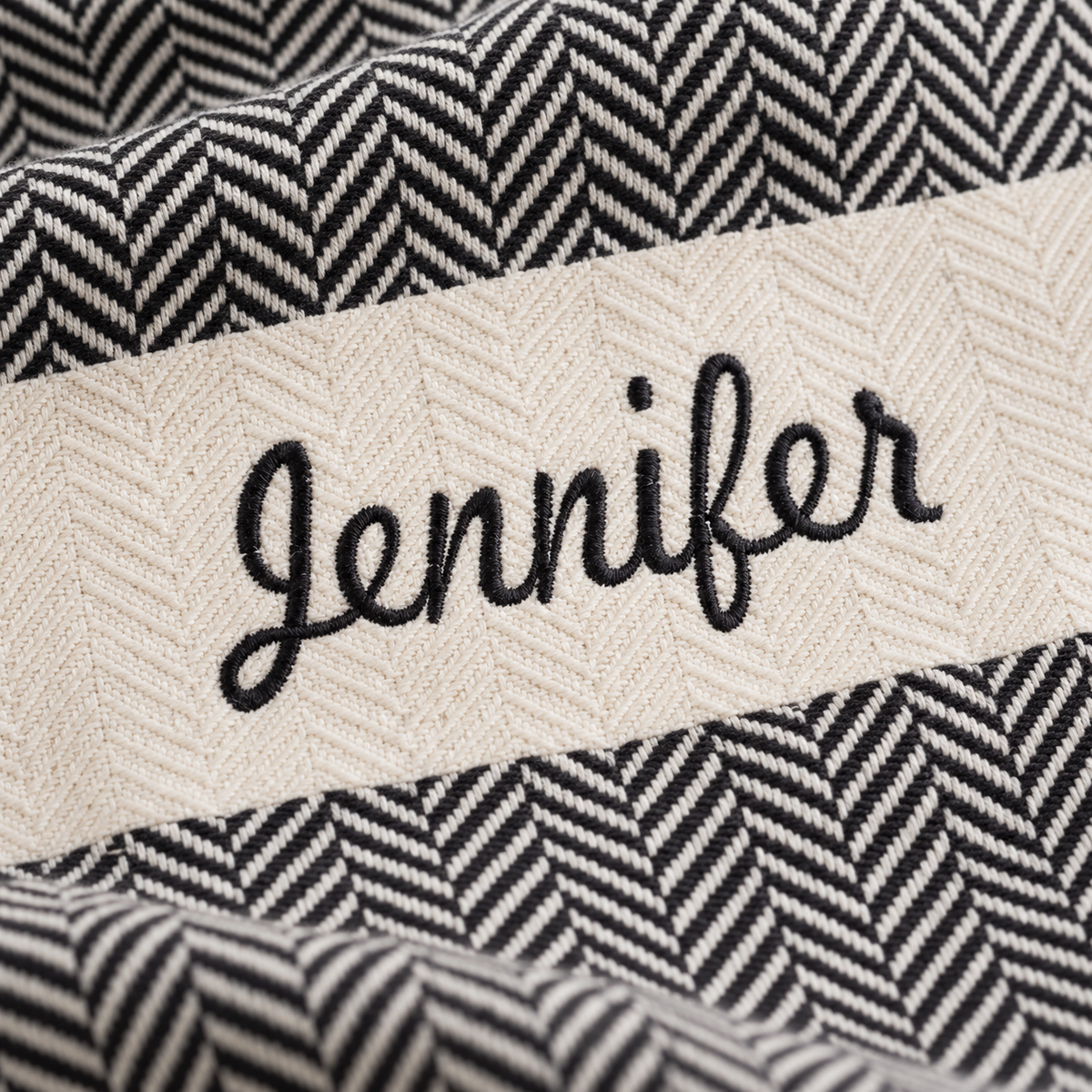 Close-up of Jennifer embroidery on a black herringbone towel